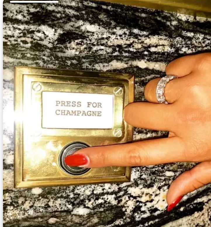 A brass call button reading press for champagne